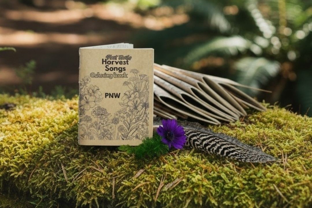 Plant Family Harvest Songs PNW coloring book resting on a mossy log in a forest, beside a feather and a purple anemone.